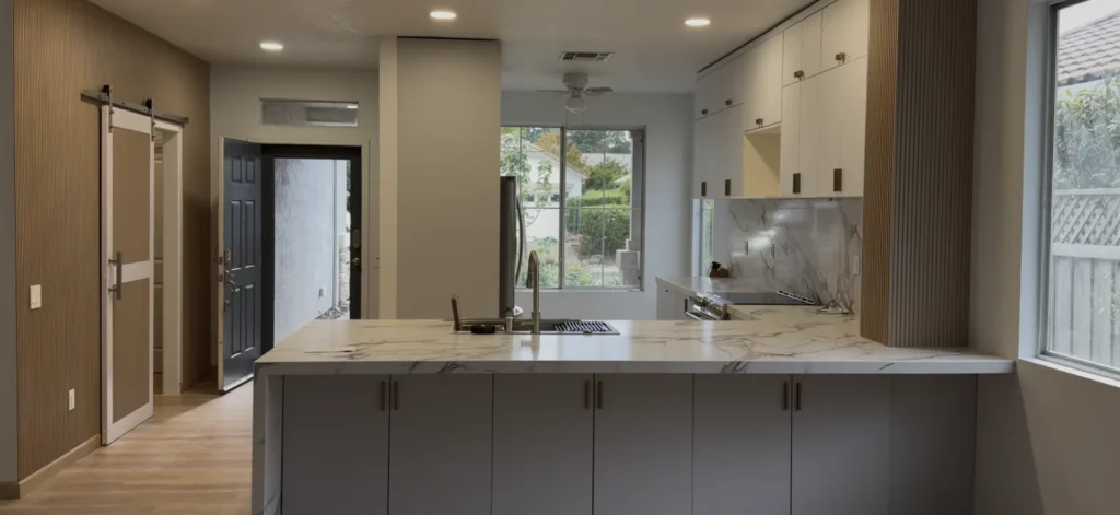 Completed open-concept kitchen remodel with a waterfall quartz island, white cabinetry, wood-slat