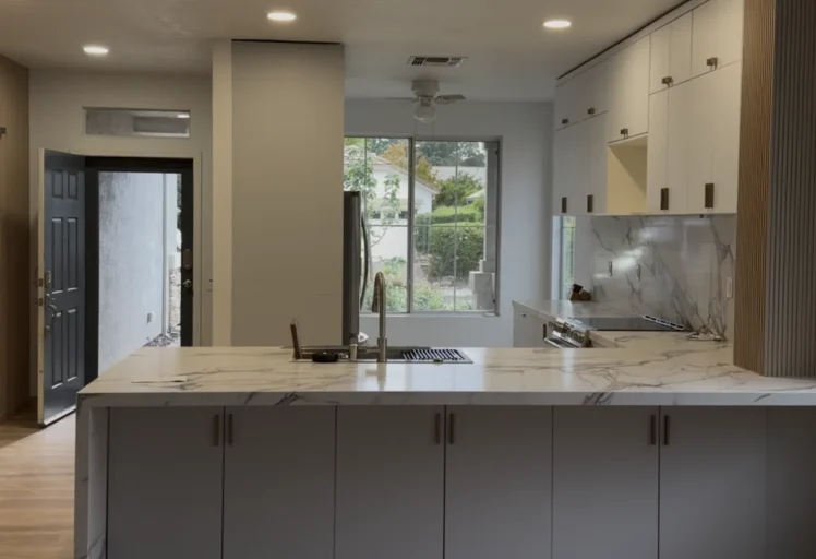 Completed open-concept kitchen remodel with a waterfall quartz island, white cabinetry, wood-slat accents, and recessed lighting in Roseville, CA.