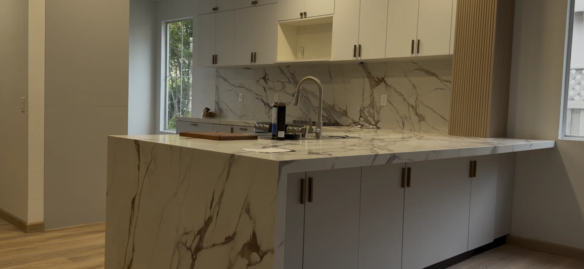 Angled view of a finished Roseville kitchen with a marble inspired quartz waterfall island and gray and white cabinetry.