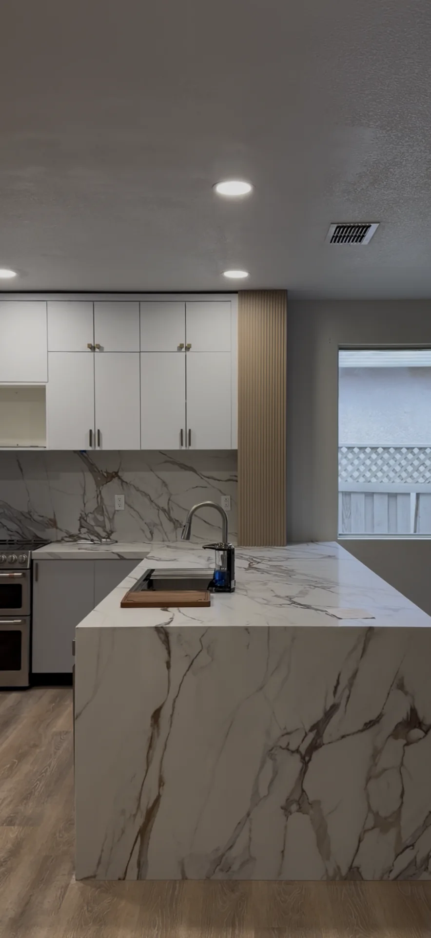 Portrait view of the completed kitchen island, quartz waterfall edge, cabinetry, and recessed lighting in Roseville, CA.