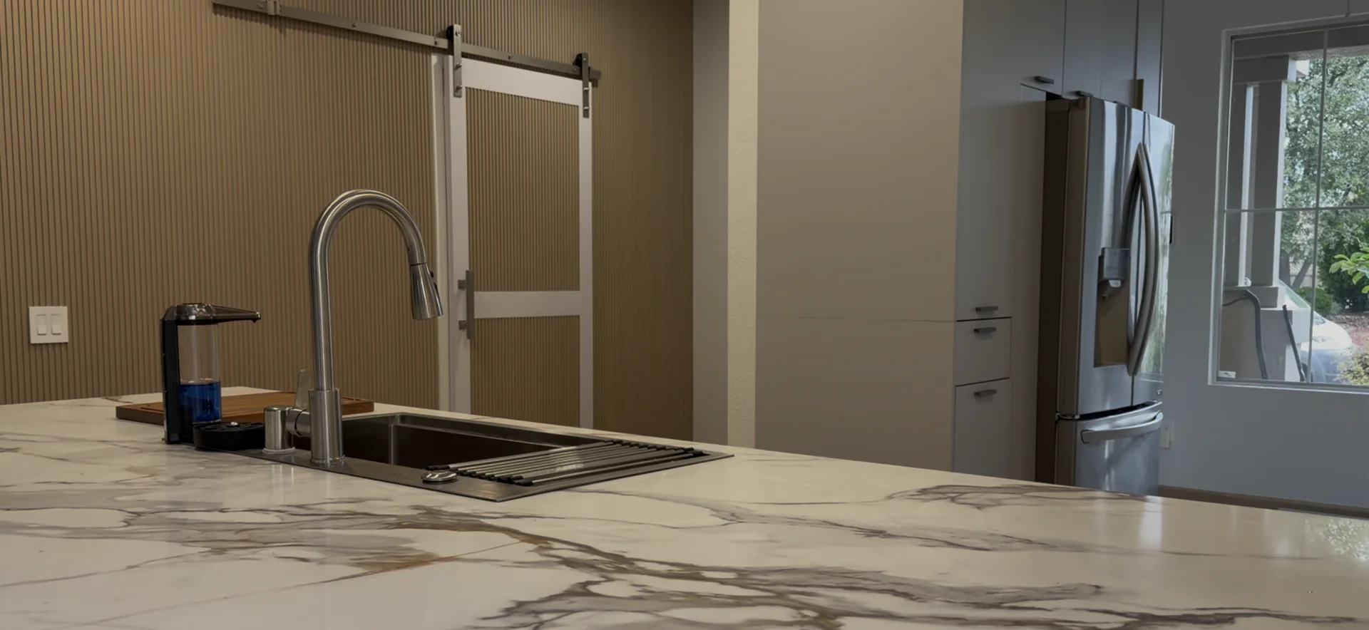 Finished kitchen sink area with marble inspired quartz counters, new cabinetry, a wood slat accent wall, and a barn door.