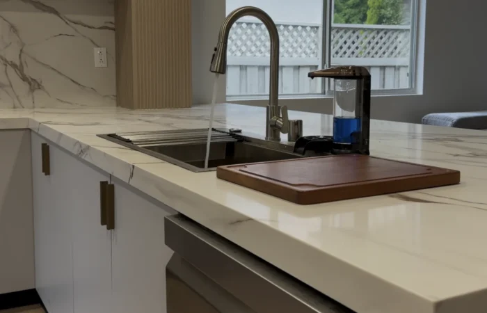 Close view of the finished kitchen sink, marble-look quartz countertop, backsplash, fixtures, and cabinetry.