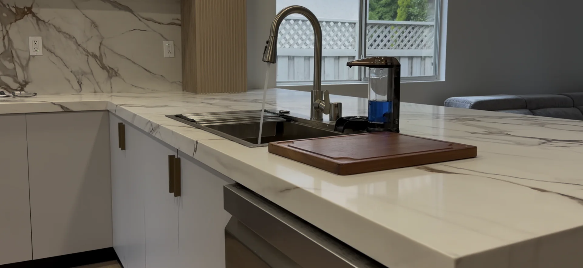 Close view of the finished kitchen sink, marble inspired quartz countertop, backsplash, fixtures, and cabinetry.