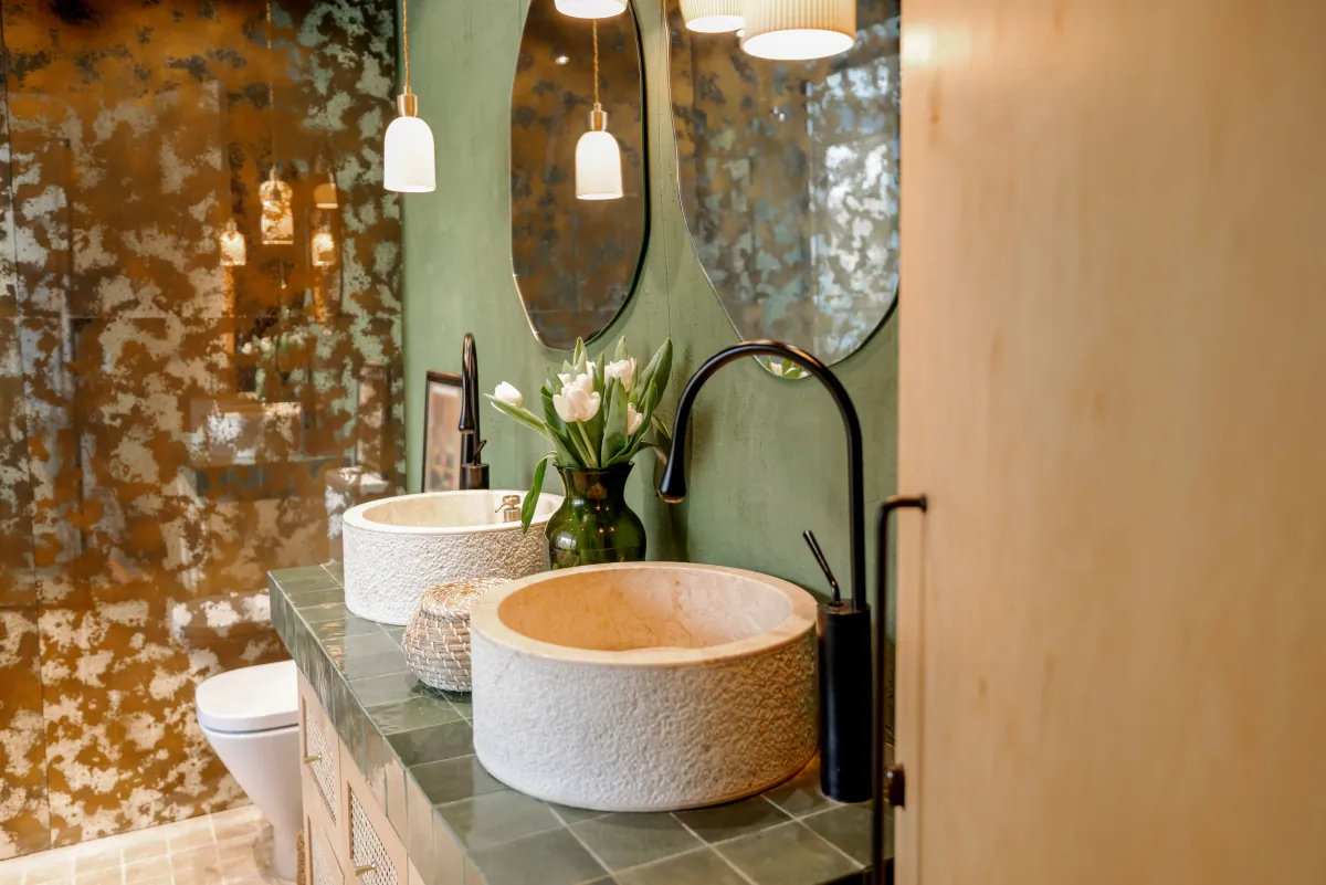 Natural bathroom palette with green cabinetry, textured vessel sinks, organic pattern and pendant lighting