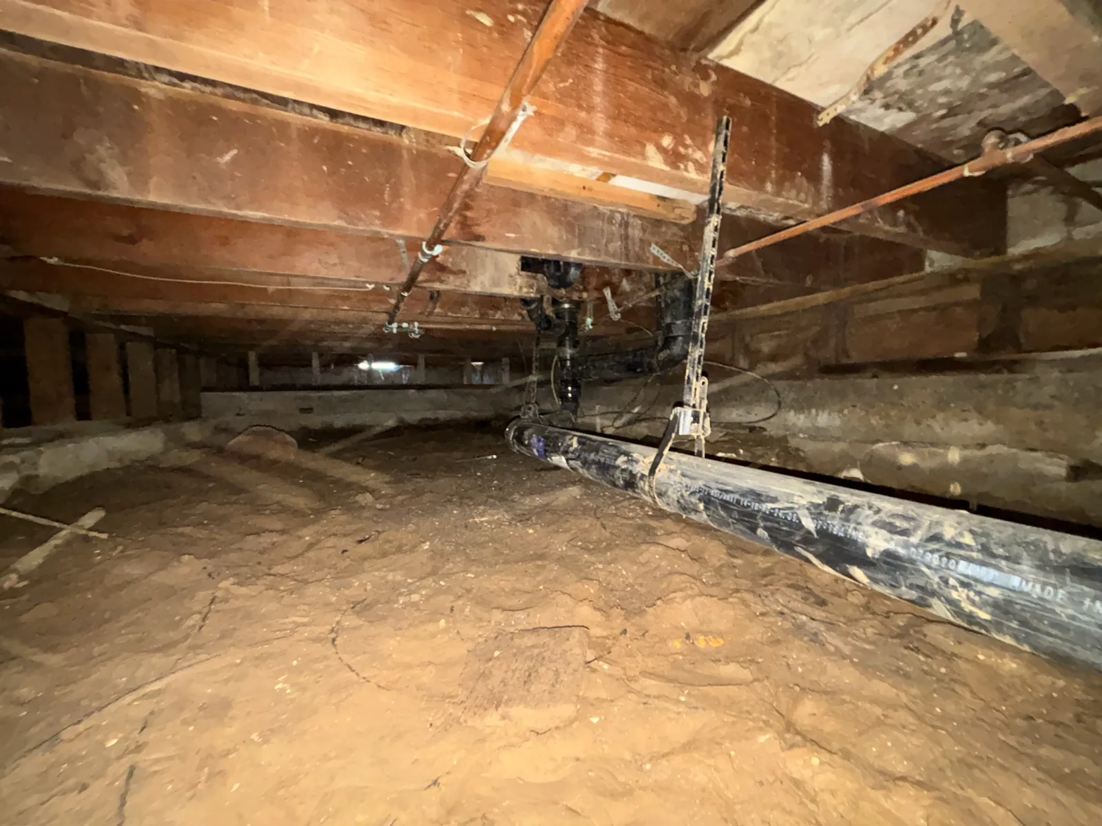 New black drain piping routed beneath floor framing in a residential crawlspace.