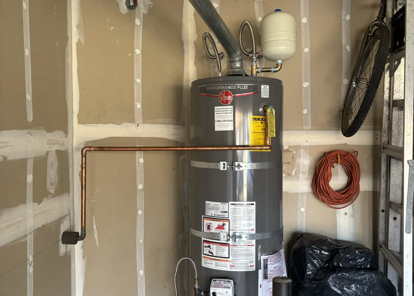 Replacement gas water heater with expansion tank, water connections, relief line, restraints, and drain pan in a Folsom garage.