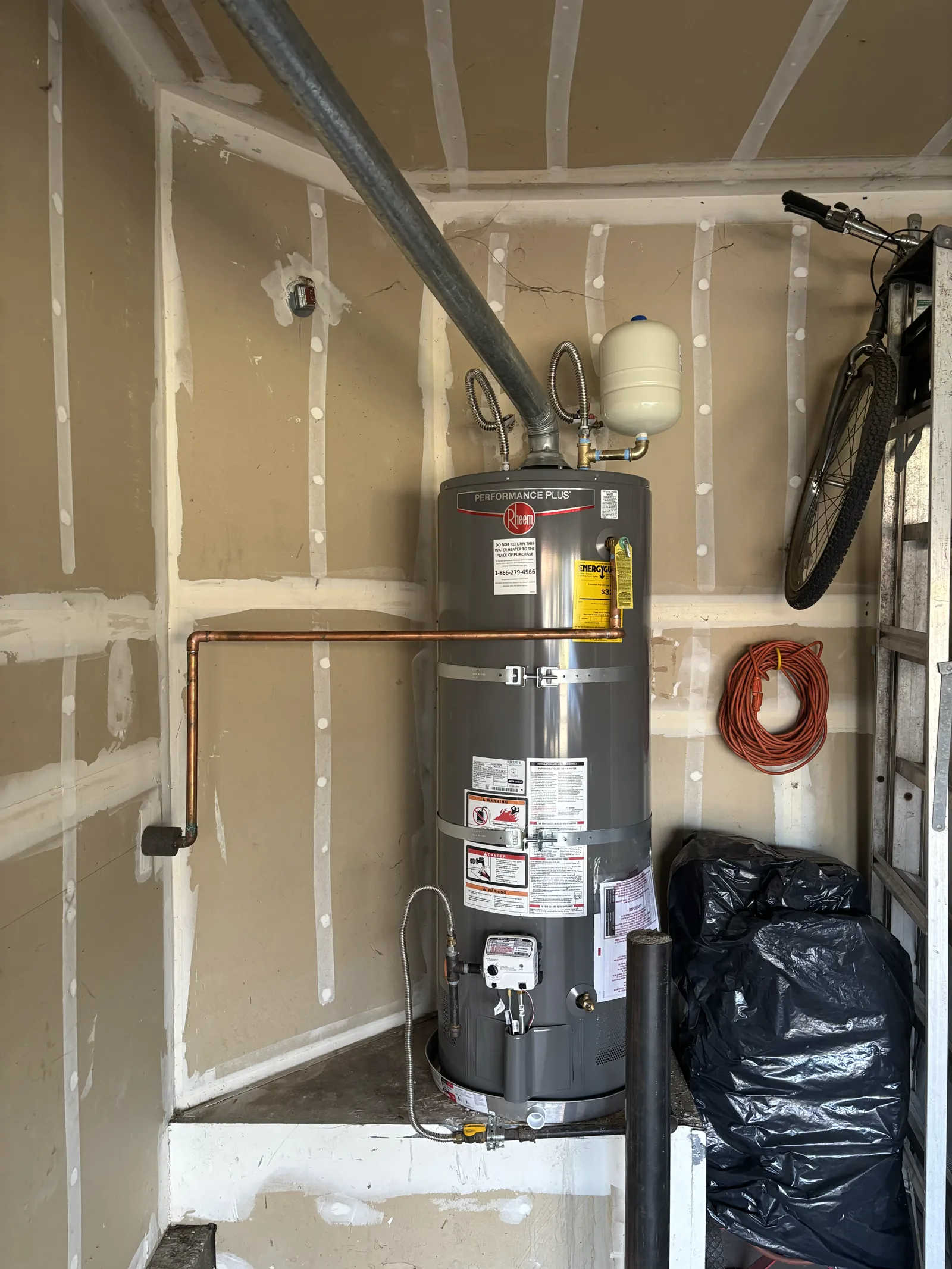 Replacement gas water heater with expansion tank, water connections, relief line, restraints, and drain pan in a Folsom garage.