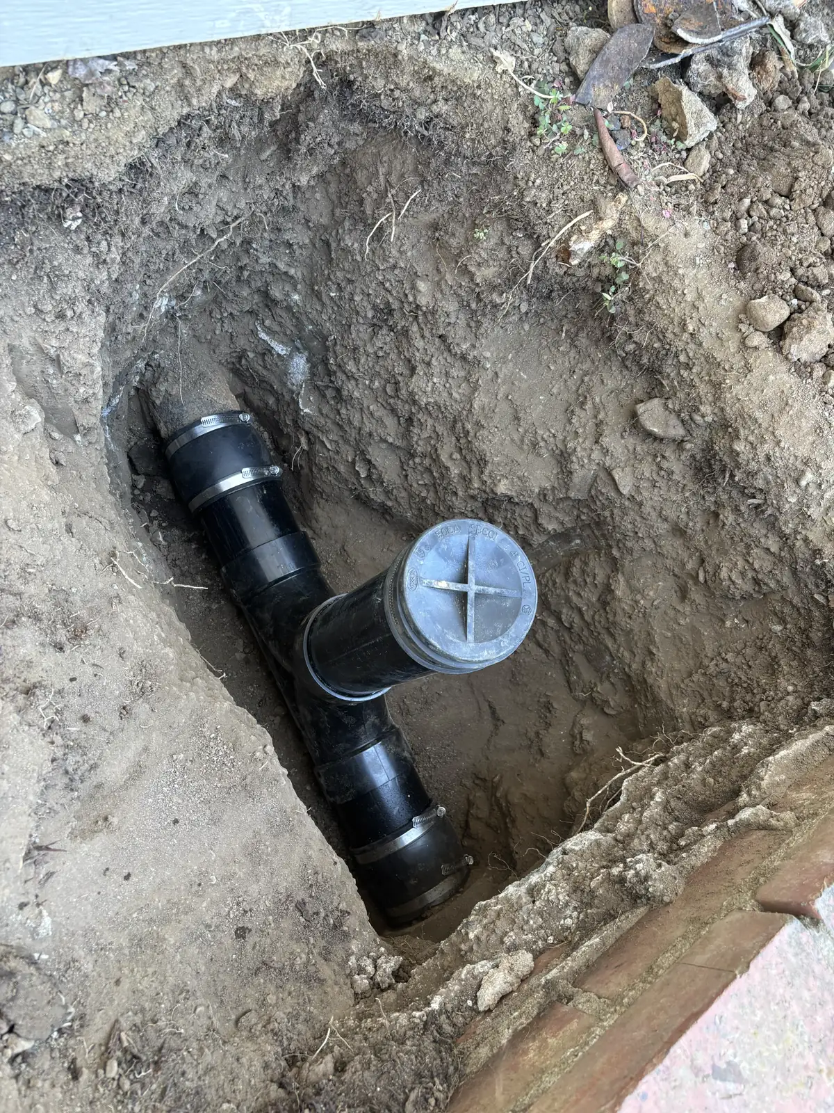 New black sewer cleanout and connected piping exposed in a residential excavation.