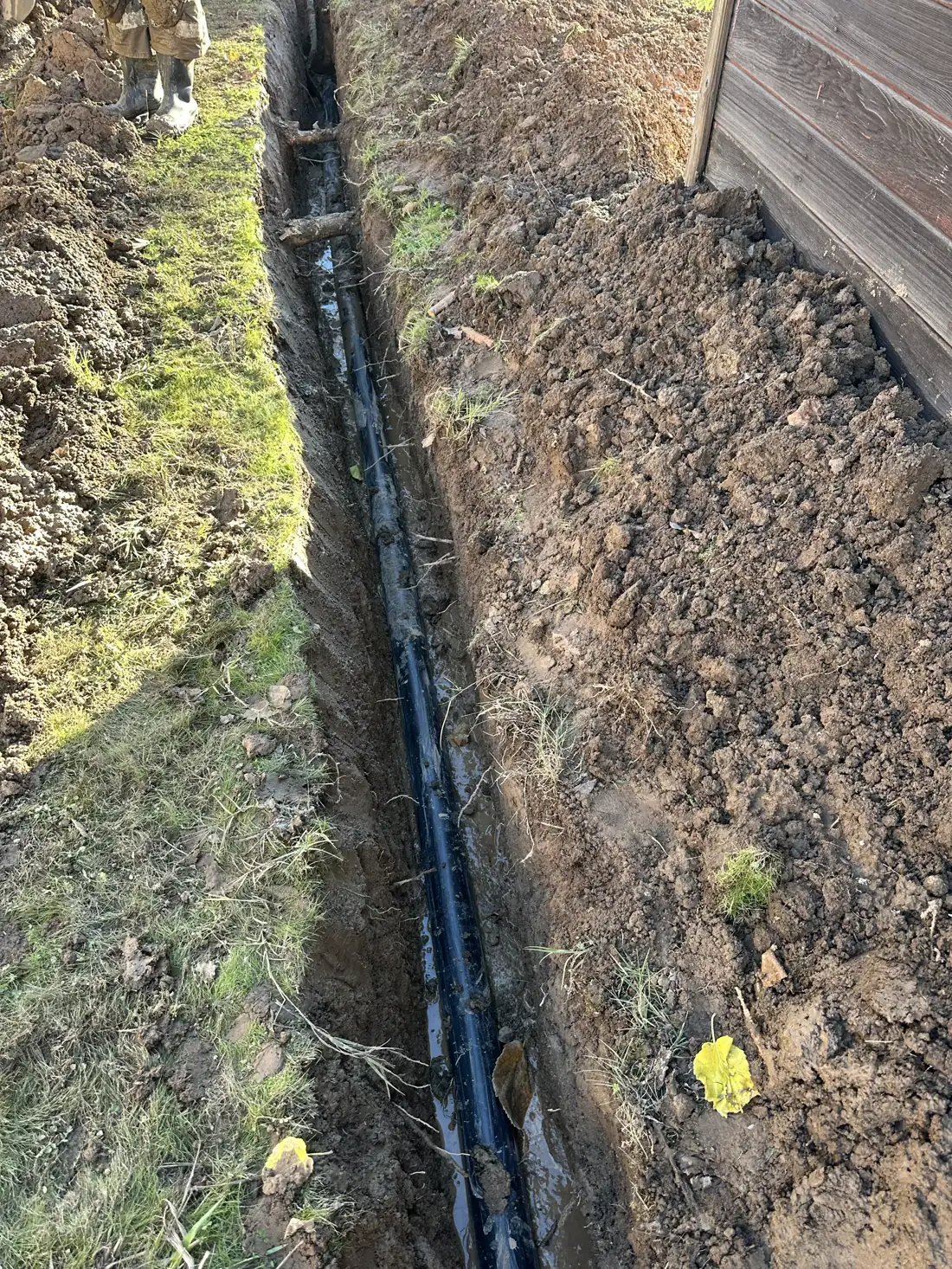 Long exterior trench with newly installed black sewer piping beside a residential structure.