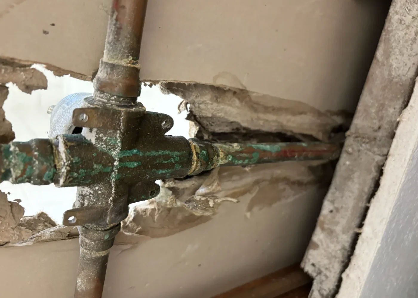 Opened residential wall showing the existing shower valve and copper piping during leak diagnosis before replacement.
