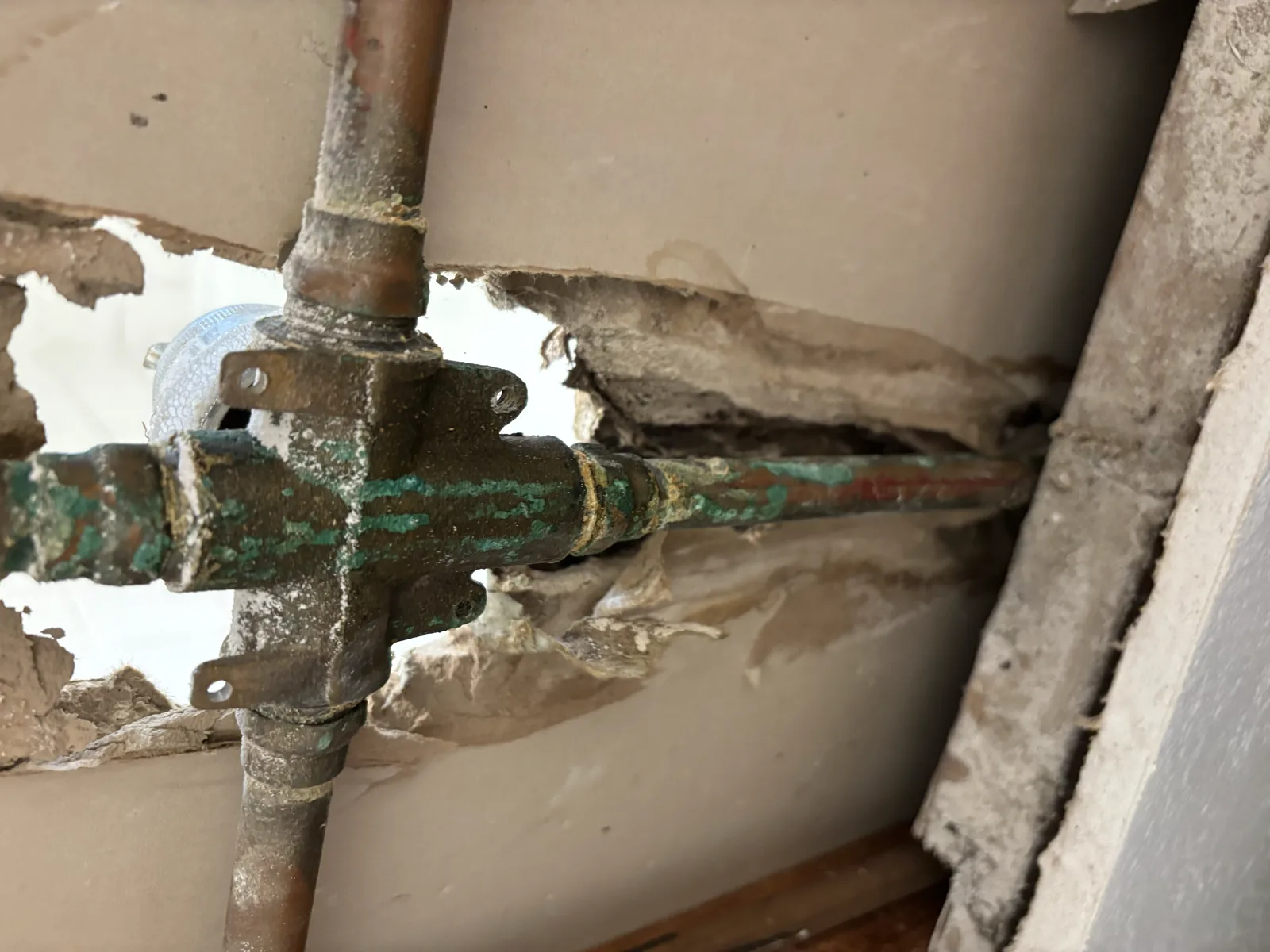Opened residential wall showing the existing shower valve and copper piping during leak diagnosis before replacement.
