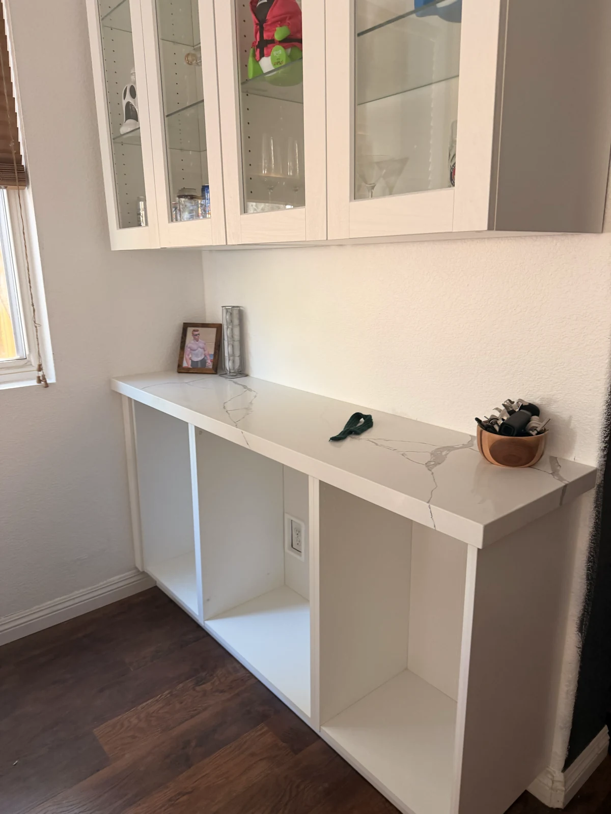 Mini bar with a white veined quartz top and open lower storage beneath a glass-front wall cabinet